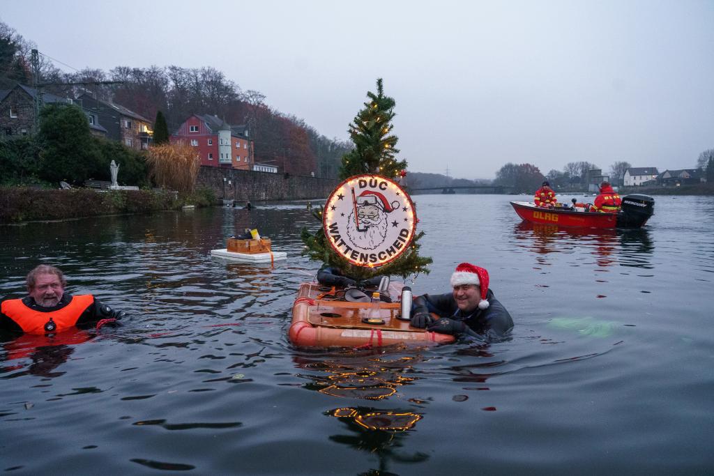 Ein Schwimmer mit Weihnachtsmütze, der  sich an einem Floß mit Weihnachtsbaum festhält